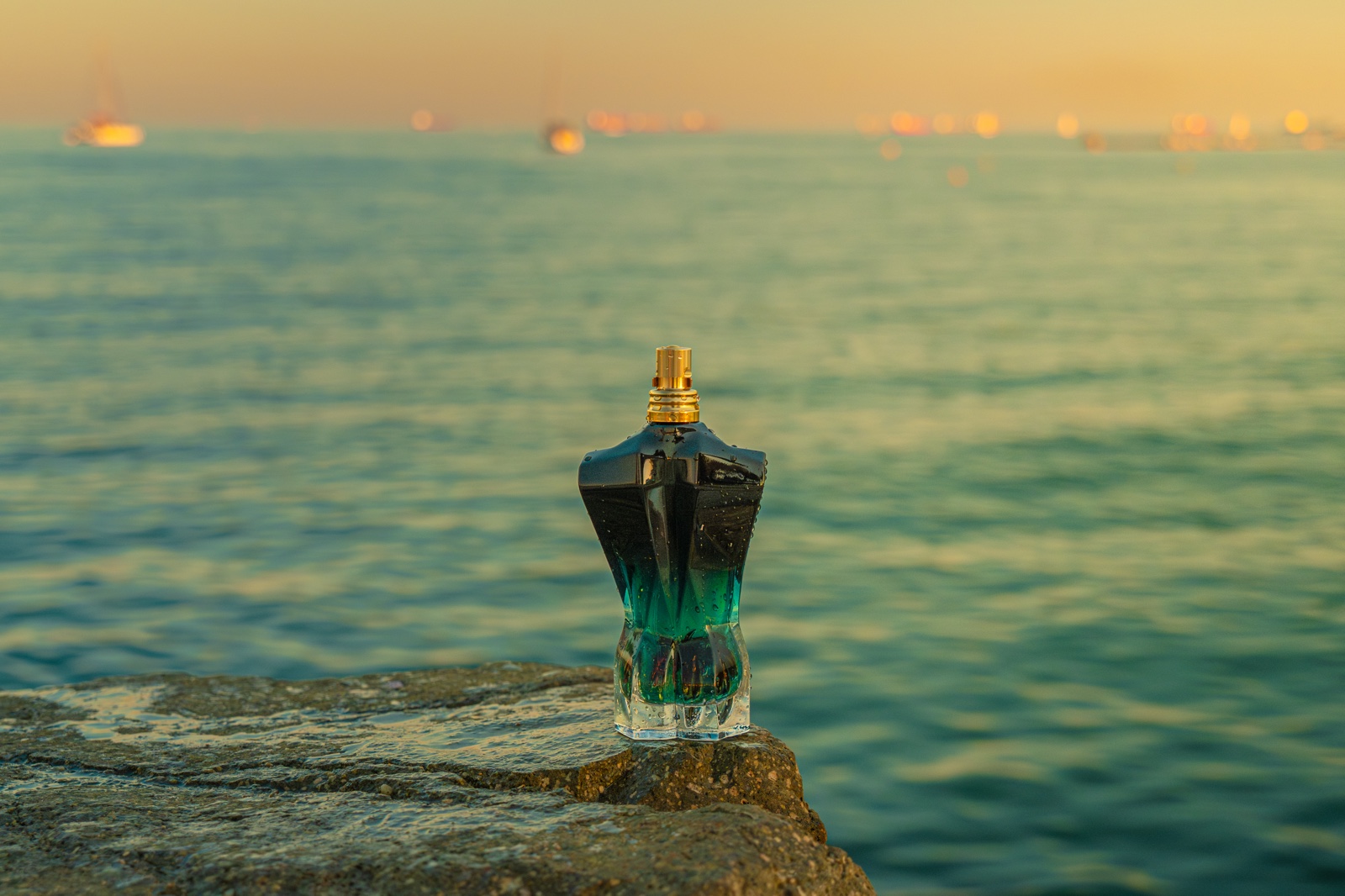 Frasco de perfume sobre una roca frente al mar al atardecer